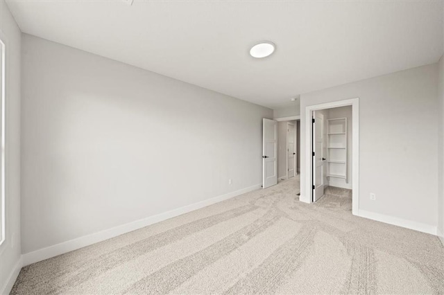 unfurnished bedroom with baseboards, a walk in closet, and light carpet