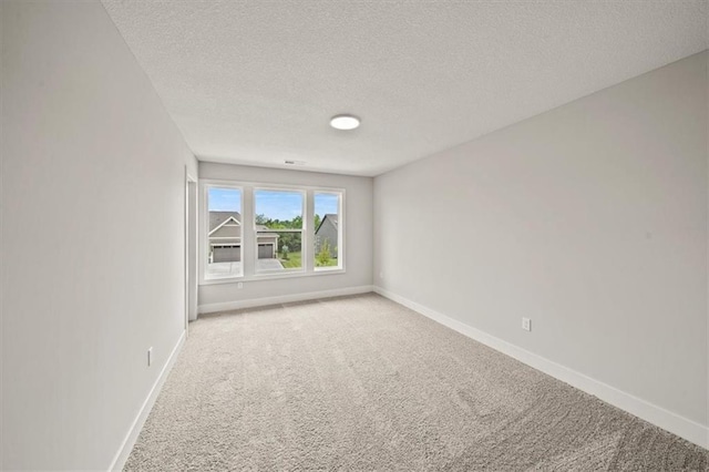 empty room with light colored carpet, a textured ceiling, and baseboards