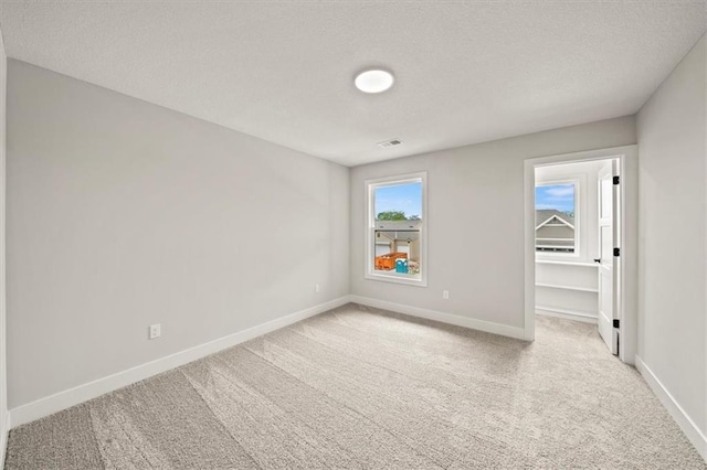empty room with a textured ceiling, baseboards, visible vents, and carpet
