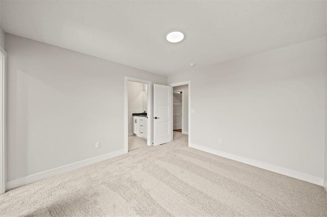 unfurnished bedroom with a closet, baseboards, a walk in closet, light colored carpet, and ensuite bath