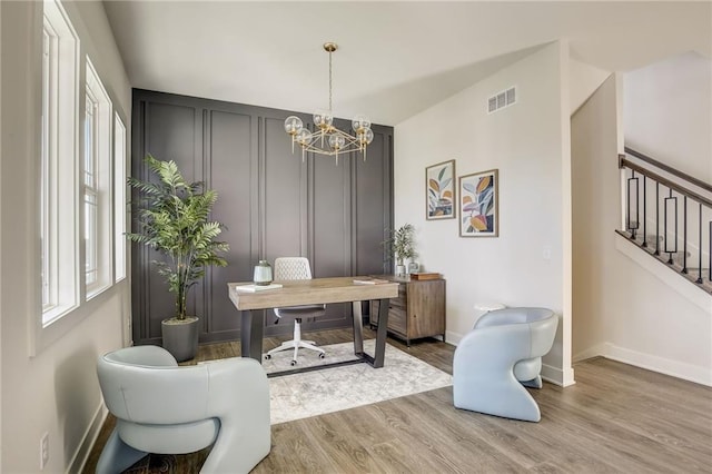 home office with visible vents, a decorative wall, wood finished floors, baseboards, and a chandelier