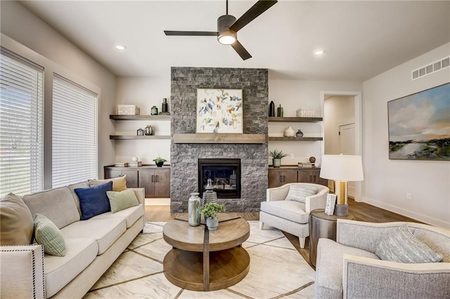 living area with a stone fireplace, light wood-style flooring, a ceiling fan, baseboards, and visible vents