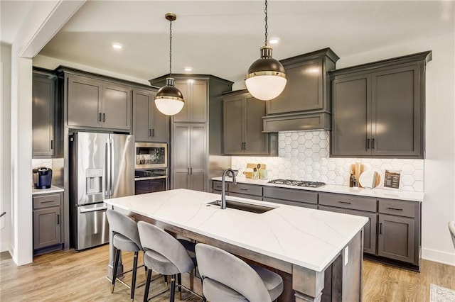 kitchen with appliances with stainless steel finishes, light stone counters, a sink, light wood-style floors, and tasteful backsplash