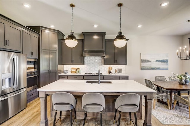 kitchen with tasteful backsplash, light stone counters, a sink, light wood finished floors, and stainless steel appliances