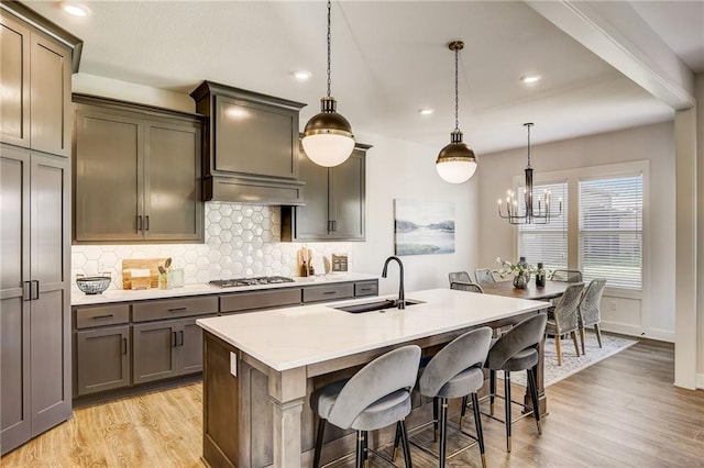 kitchen with stainless steel gas cooktop, light wood-type flooring, tasteful backsplash, a sink, and a notable chandelier