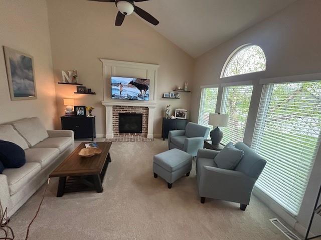 carpeted living area featuring high vaulted ceiling, a ceiling fan, a brick fireplace, and visible vents