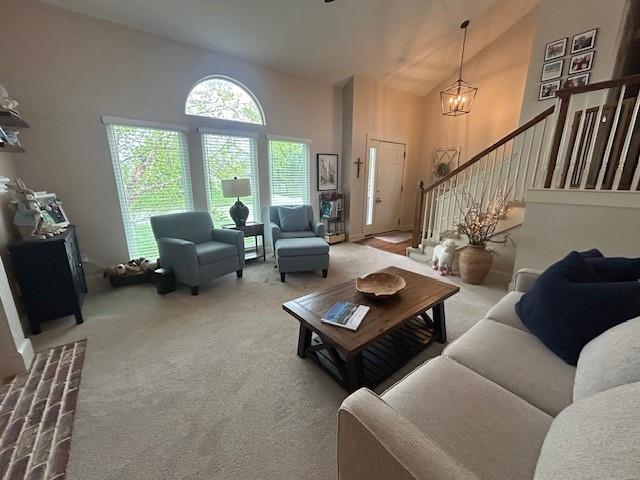carpeted living area with an inviting chandelier, high vaulted ceiling, and stairway