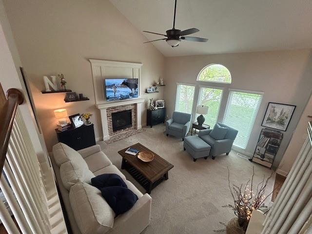 living area featuring high vaulted ceiling, a fireplace, a ceiling fan, and light colored carpet