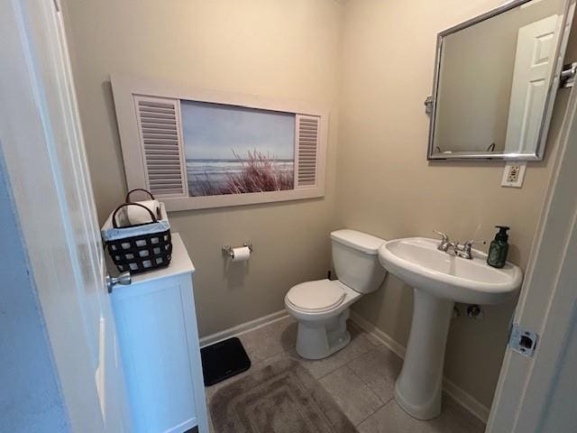 half bathroom with toilet, tile patterned floors, a sink, and baseboards