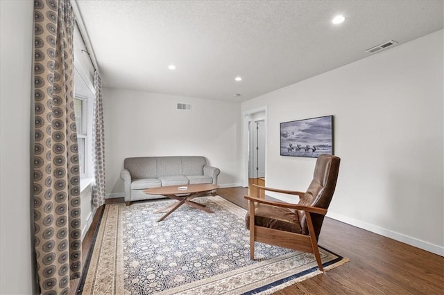 living area featuring visible vents, a textured ceiling, baseboards, and wood finished floors