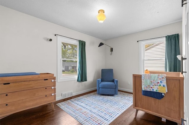 bedroom with visible vents, a textured ceiling, baseboards, and wood finished floors