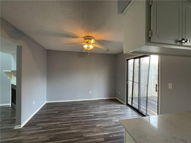 unfurnished dining area featuring a ceiling fan, a textured ceiling, dark wood-style floors, and a fireplace
