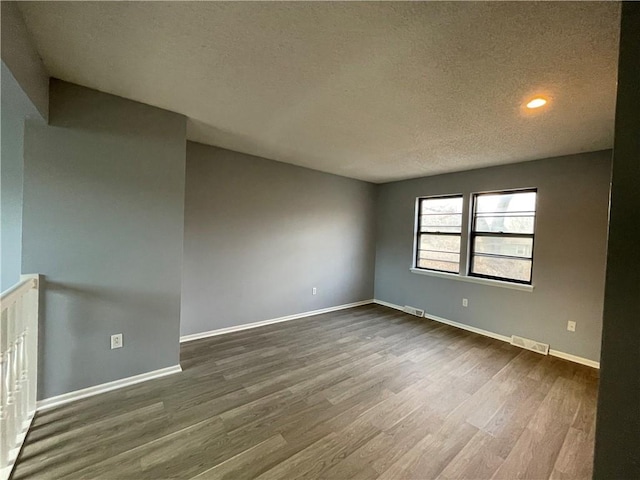 spare room with a textured ceiling, visible vents, dark wood-style floors, and baseboards