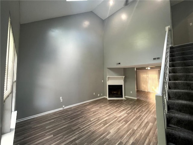 unfurnished living room with visible vents, stairs, dark wood-style floors, high vaulted ceiling, and a fireplace with flush hearth