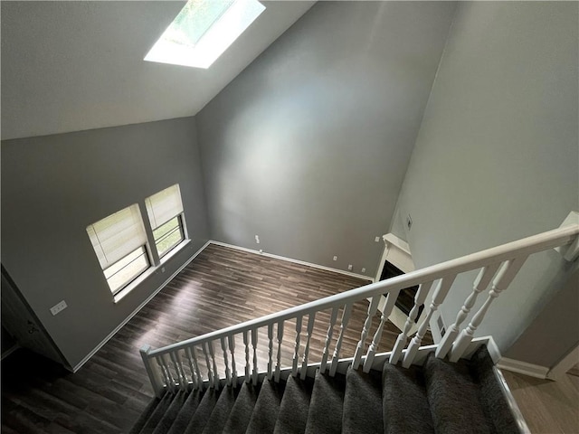 stairs featuring baseboards, lofted ceiling with skylight, and wood finished floors