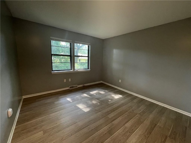 empty room with baseboards, dark wood finished floors, and visible vents
