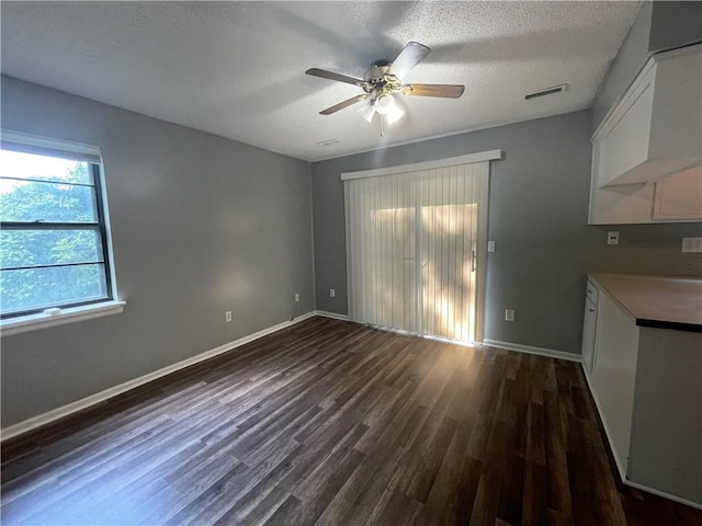 unfurnished dining area featuring a ceiling fan, a textured ceiling, visible vents, baseboards, and dark wood-style floors