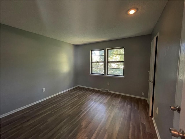 empty room with baseboards, visible vents, and dark wood finished floors