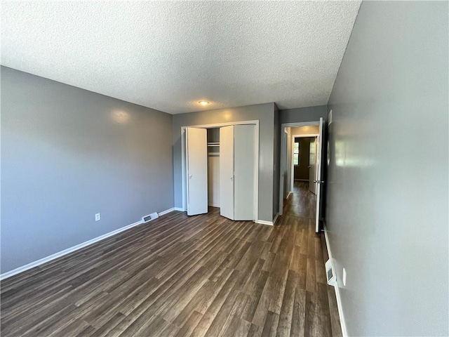 unfurnished bedroom featuring dark wood-style flooring, a textured ceiling, baseboards, visible vents, and a closet