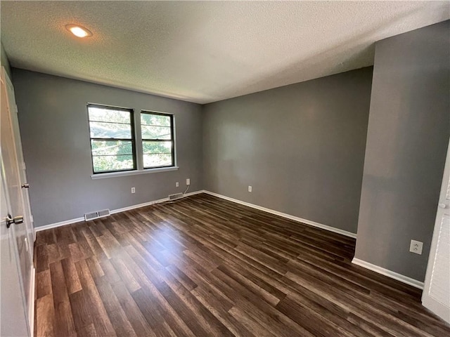 spare room with baseboards, dark wood finished floors, a textured ceiling, and visible vents