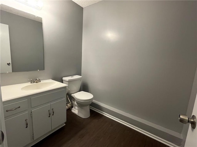 half bathroom with a textured ceiling, wood finished floors, vanity, baseboards, and toilet
