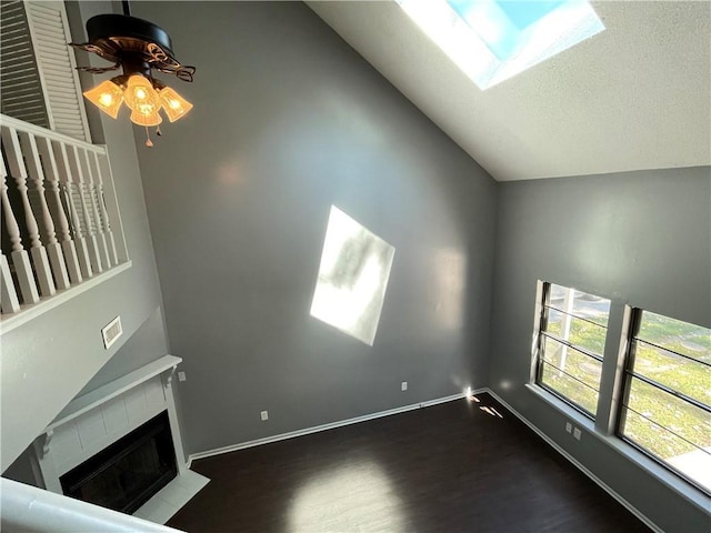unfurnished living room featuring ceiling fan, baseboards, wood finished floors, a tile fireplace, and lofted ceiling with skylight