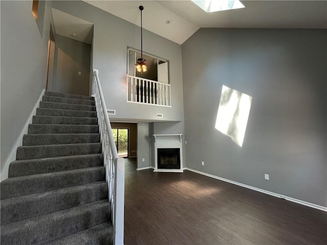 staircase with a fireplace, high vaulted ceiling, baseboards, wood finished floors, and a skylight
