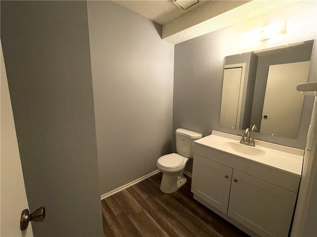 half bathroom with a textured ceiling, wood finished floors, vanity, baseboards, and toilet