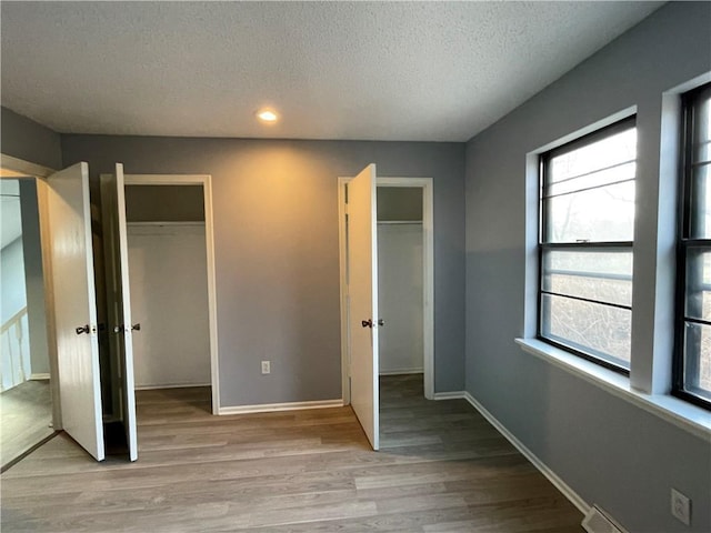 unfurnished bedroom featuring light wood-style floors, two closets, recessed lighting, and a textured ceiling