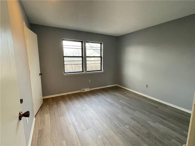 empty room with visible vents, a textured ceiling, baseboards, and dark wood-style floors