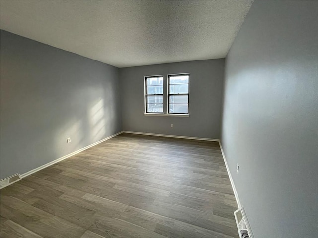 empty room featuring baseboards, a textured ceiling, visible vents, and wood finished floors