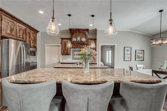 kitchen featuring crown molding, light stone countertops, a breakfast bar area, appliances with stainless steel finishes, and hanging light fixtures