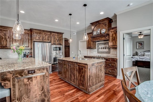 kitchen with backsplash, wood finished floors, a sink, stainless steel appliances, and an island with sink