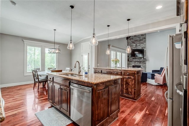 kitchen with dark wood-style floors, appliances with stainless steel finishes, a center island with sink, and a sink