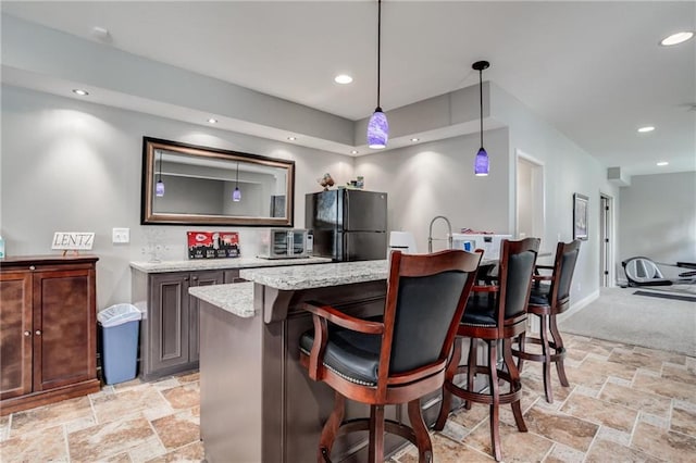 bar featuring hanging light fixtures, indoor wet bar, freestanding refrigerator, recessed lighting, and stone tile floors