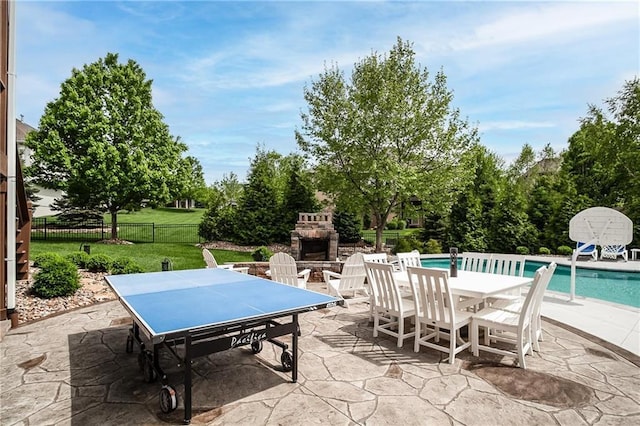 view of patio with an outdoor stone fireplace, an outdoor pool, fence, and outdoor dining space