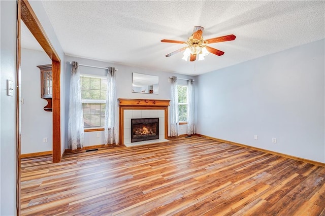unfurnished living room with a textured ceiling, wood finished floors, a ceiling fan, a tile fireplace, and baseboards