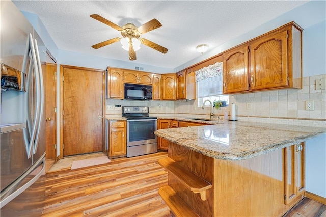 kitchen with stainless steel appliances, a sink, a peninsula, light wood-style floors, and brown cabinetry