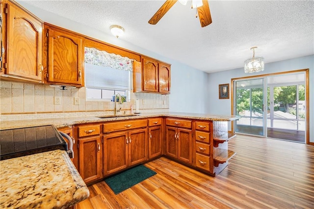 kitchen featuring a peninsula, a sink, brown cabinets, a textured ceiling, and decorative backsplash