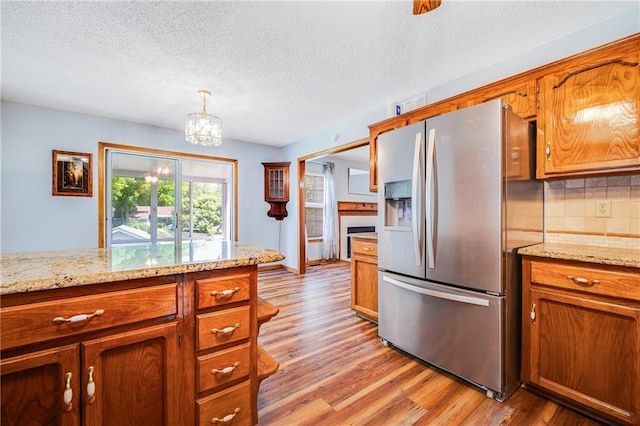 kitchen with stainless steel refrigerator with ice dispenser, light wood-style flooring, brown cabinets, and a textured ceiling