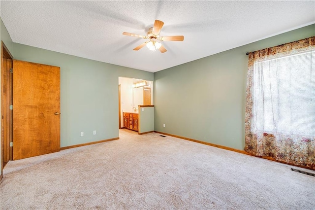 unfurnished bedroom featuring light colored carpet, baseboards, a textured ceiling, connected bathroom, and ceiling fan
