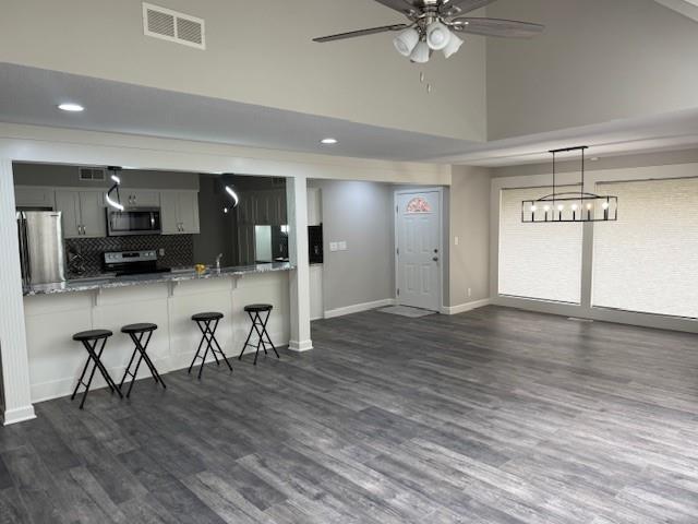 kitchen with appliances with stainless steel finishes, ceiling fan, visible vents, a kitchen breakfast bar, and high vaulted ceiling