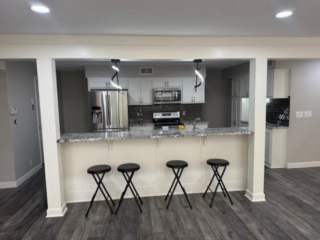 kitchen with a peninsula, baseboards, appliances with stainless steel finishes, and tasteful backsplash