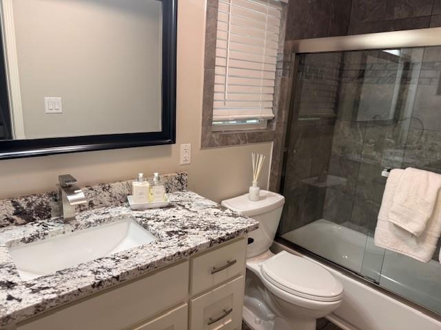 bathroom with combined bath / shower with glass door, toilet, and vanity