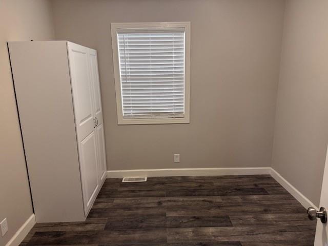 unfurnished room with baseboards, visible vents, and dark wood-style floors