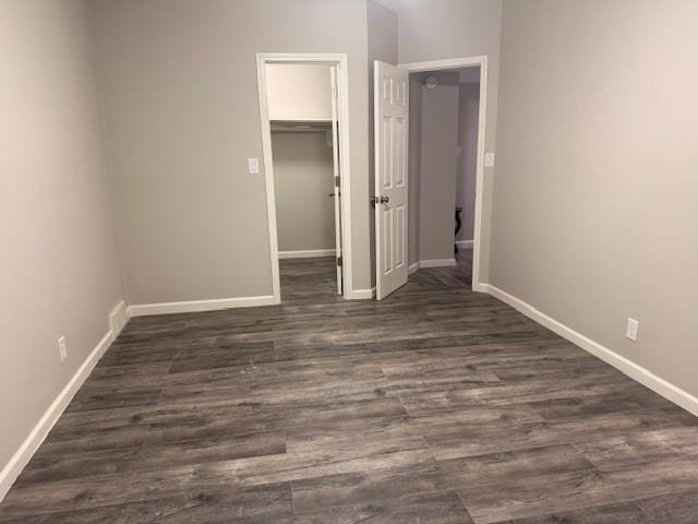 unfurnished bedroom featuring baseboards, a closet, a walk in closet, and dark wood-type flooring
