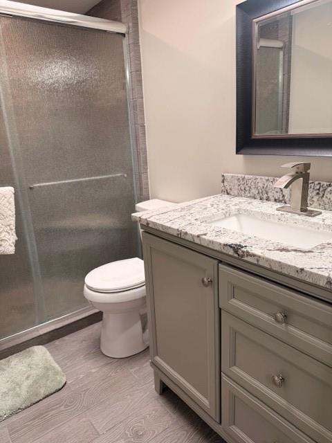 bathroom featuring toilet, wood finished floors, vanity, and a stall shower