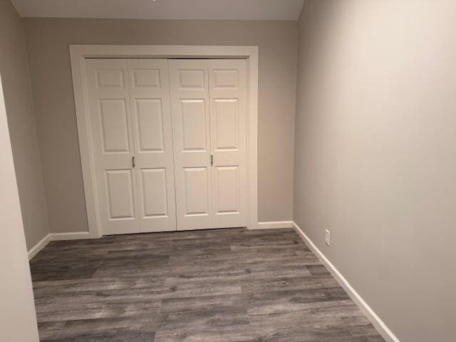 unfurnished bedroom with baseboards, dark wood-style flooring, and a closet
