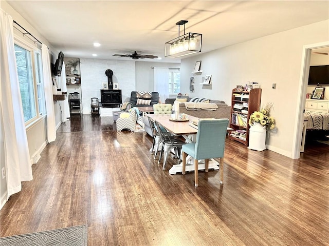 dining area featuring baseboards, a wood stove, a ceiling fan, and wood finished floors