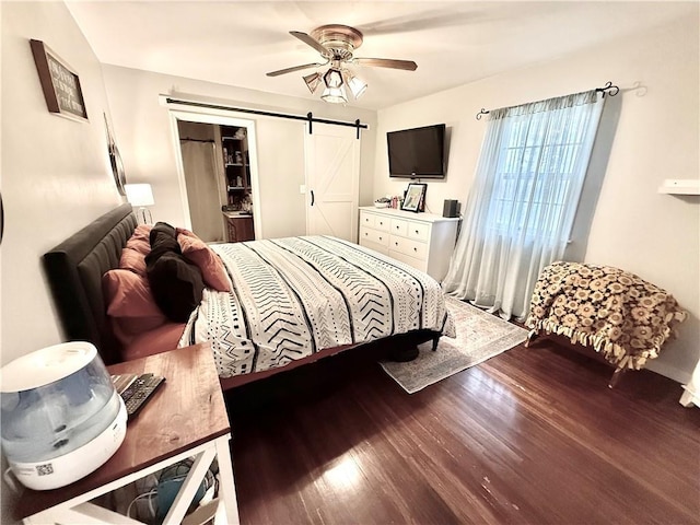 bedroom with a ceiling fan, a barn door, and wood finished floors